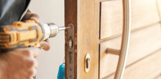 a diyer who has answered the question of how do you fix a door lock and is doing the repairs with a drill