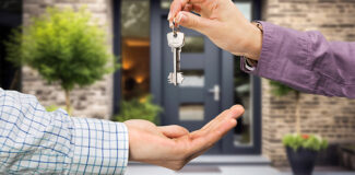 a close up of two people exchanging keys in front of a modern property from a master keying system