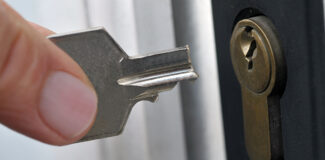a close up of a key broken in a lock as a homeowner holds the main part wondering how to get a broken key out of a lock