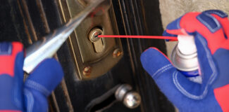 a close up of a homeowner lubricating a door lock